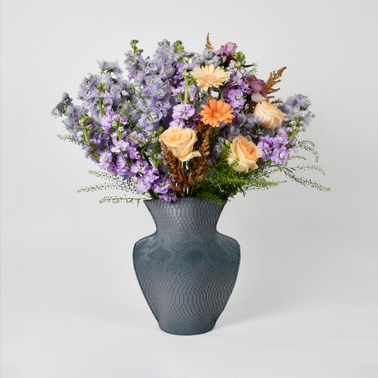 purple and peach flowers arrangement in grey leather vase