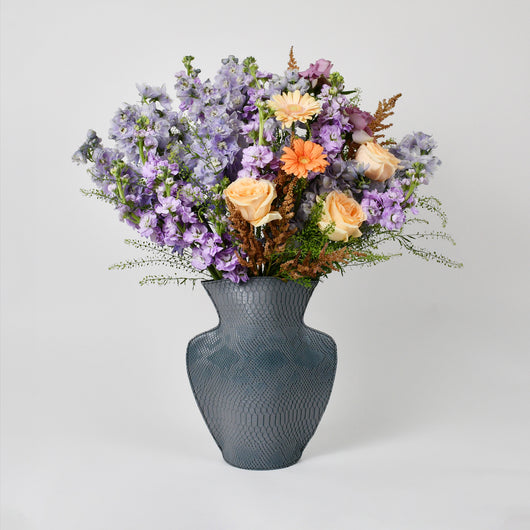 purple and peach flowers arrangement in grey leather vase